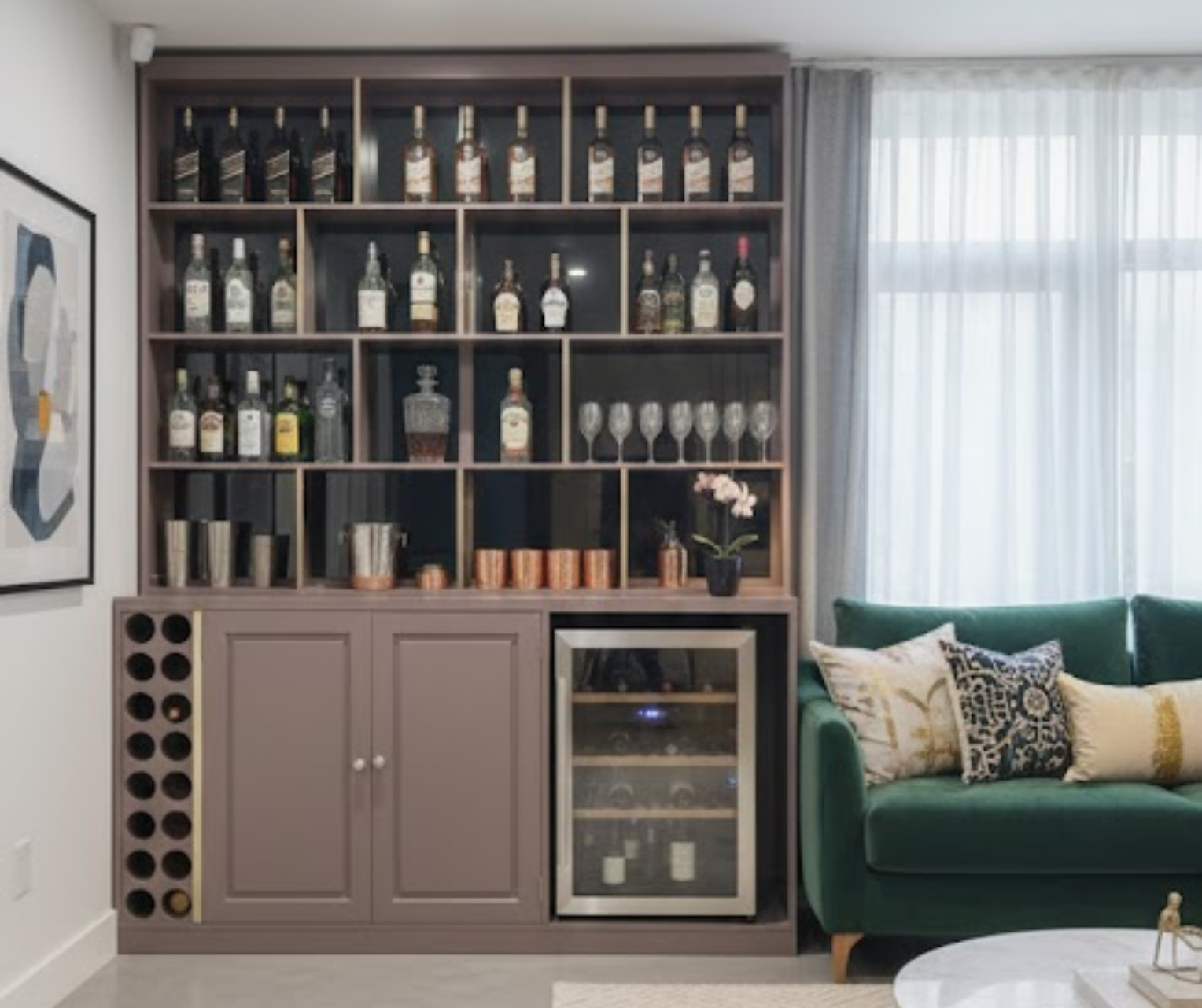 Modern living room with a large bookshelf displaying bottles and glasses, a green sofa, and a wine cooler.
